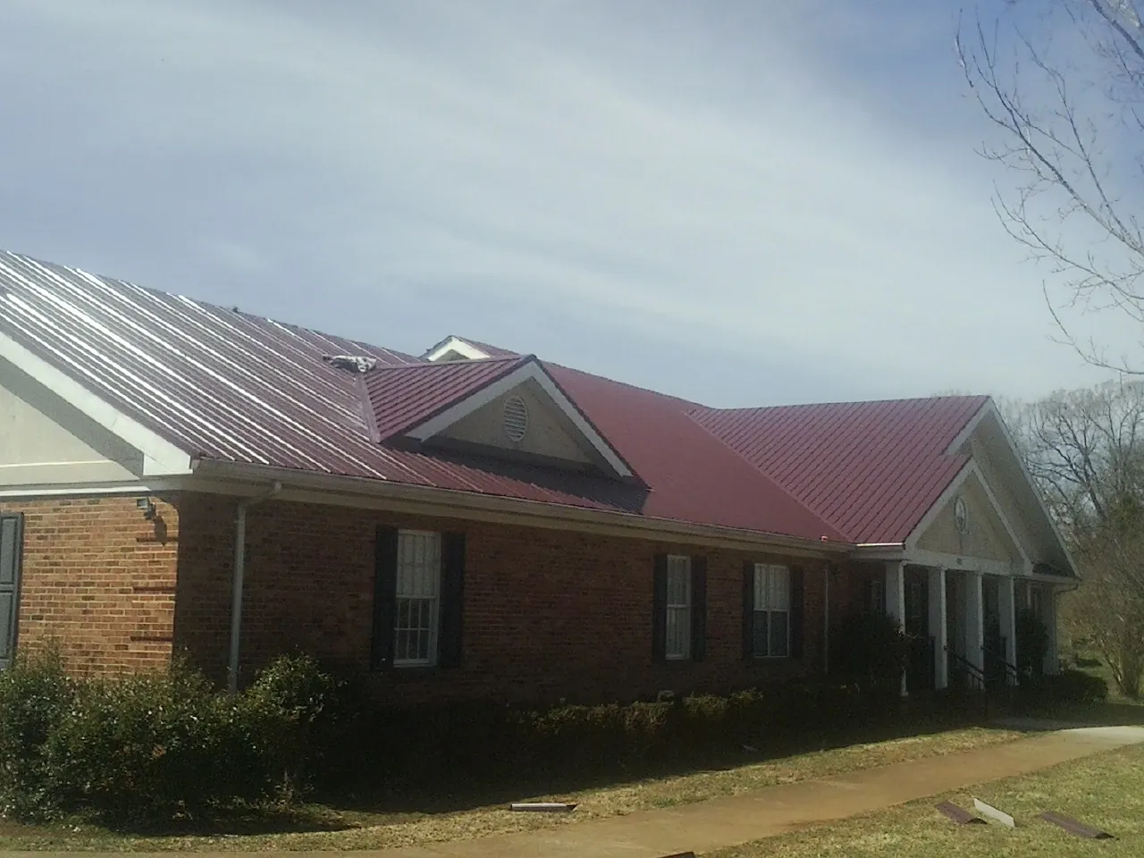 Red metal roof with gabled entries on a long brick building, from a Hail Damage Roof Repair job in Saint Simons Island