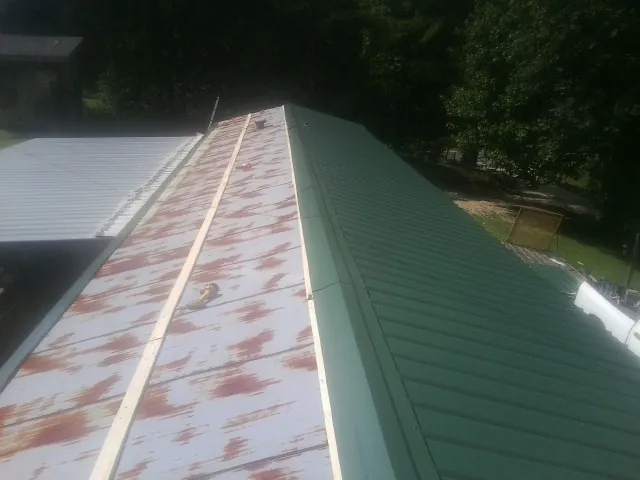 Old rusted panels beside newly installed green metal roofing — Wind Damage Roof Repair by Roofing Brothers in Saint Simons Island
