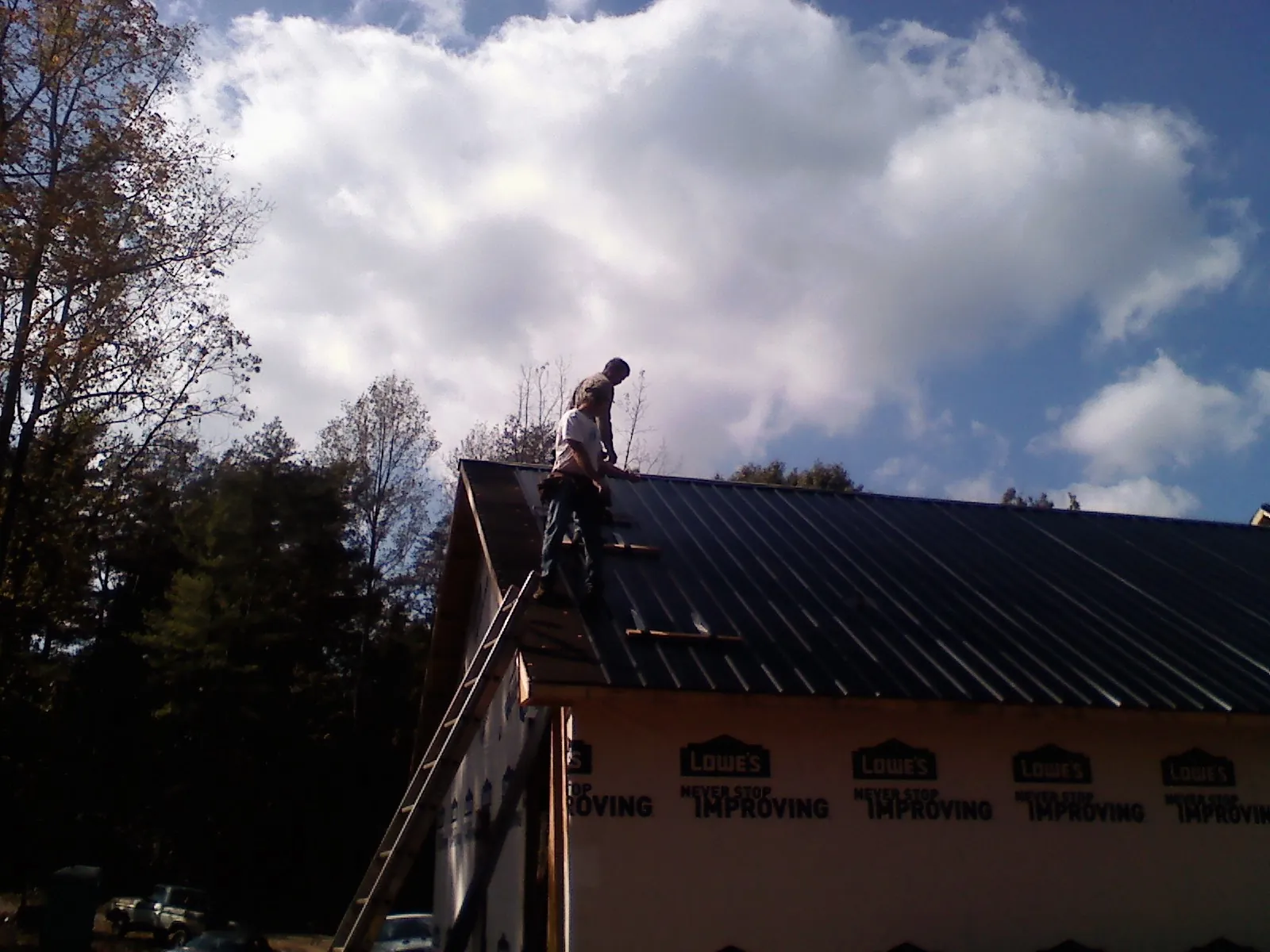 Roofer fastening dark metal panels high against a cloudy sky, from a Roof Inspection job in Saint Simons Island