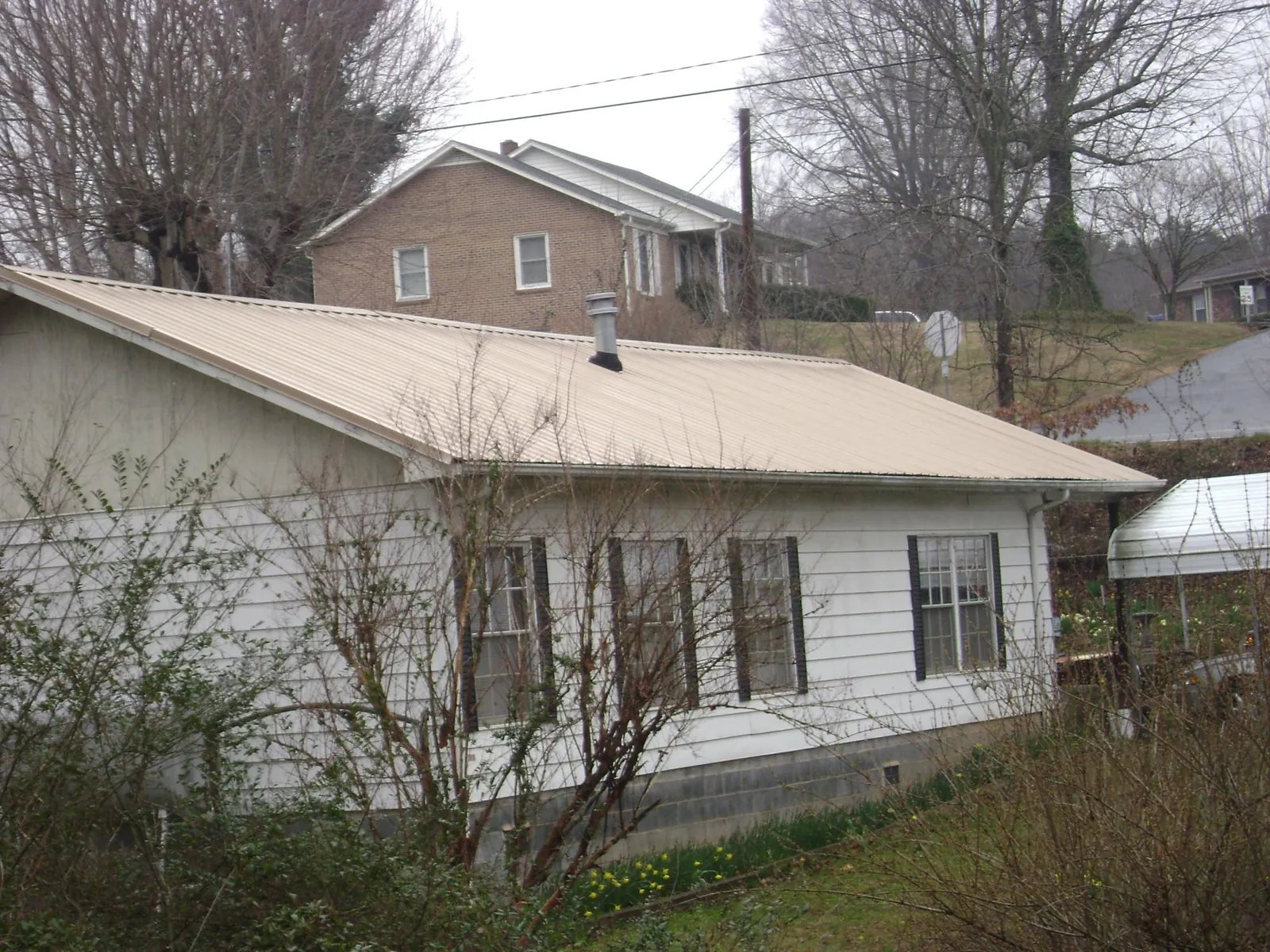 Tan metal roof on a white sided house set into a hillside — Commercial Roofing by Roofing Brothers in Saint Simons Island