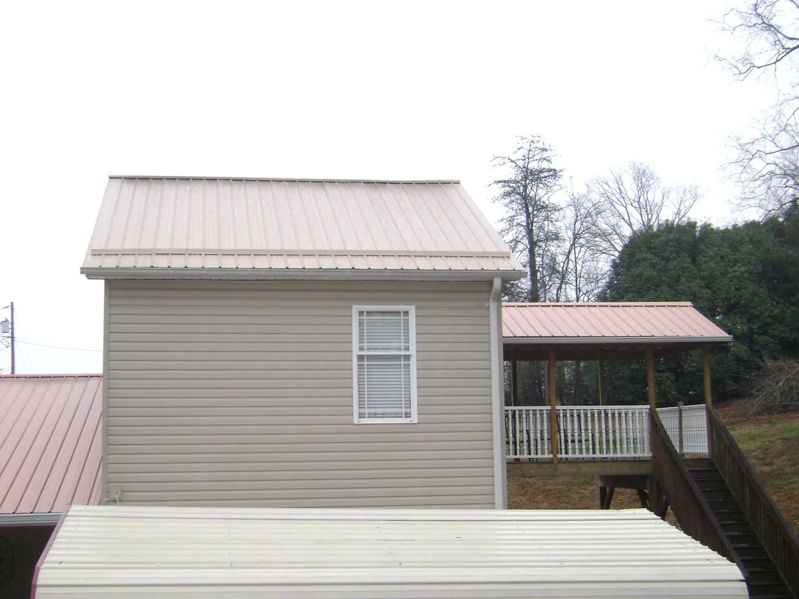 Tan metal roofs on a two story addition and attached porch, from a Roof Replacement job in Saint Simons Island